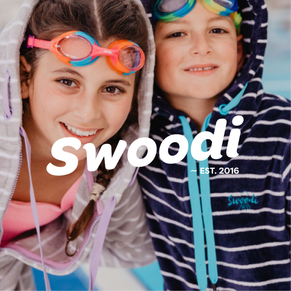 A photo of two children wearing Swoodi hooded towels, with a white Swoodi logo